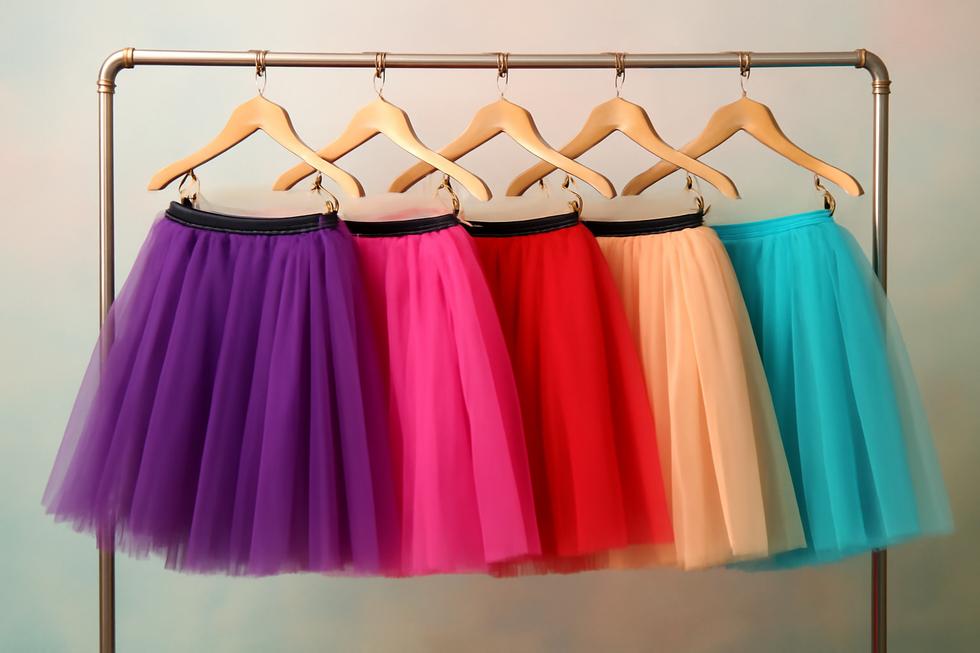 A rack displaying different styles and colors of adult tutu skirts against a serene pastel backdrop.